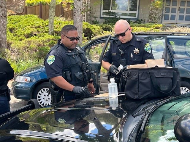 Officers by hood of vehicle with evidence in hands. 